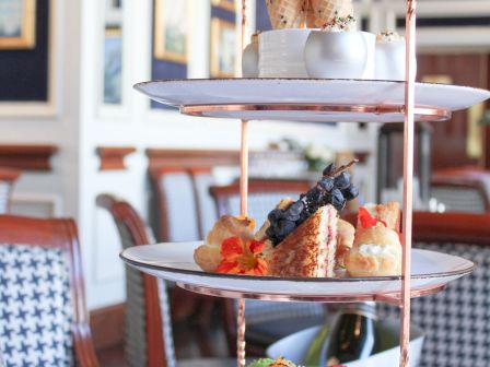 A three-tiered stand with assorted pastries and sweets is displayed in a dining setting, featuring colorful macarons and desserts.