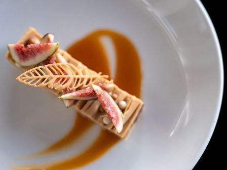 A plated dessert featuring figs, caramel sauce, and intricate wafer decoration on a white plate.