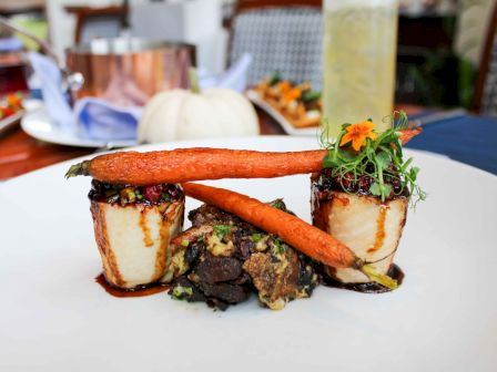 The image shows a gourmet dish with roasted carrots, rolled vegetables, greens, and a drizzle of sauce arranged on a white plate.