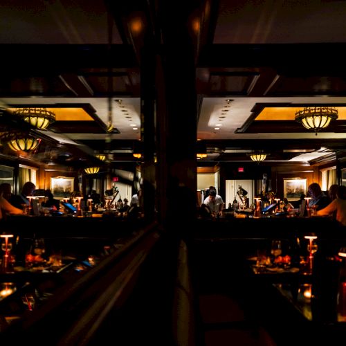 A dimly lit restaurant scene with patrons seated at tables, reflected in a mirror, warm lighting creates a cozy ambiance.