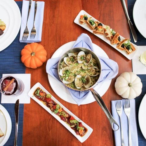 The image shows a table with various dishes, drinks, and decorative mini pumpkins set for a meal on wooden surface with blue placemats.