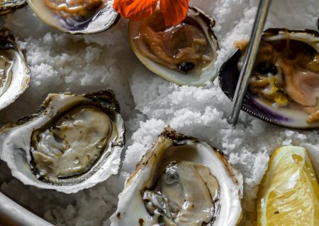 An arrangement of oysters and other shellfish on ice, garnished with an orange flower and a lemon wedge, served on a platter.