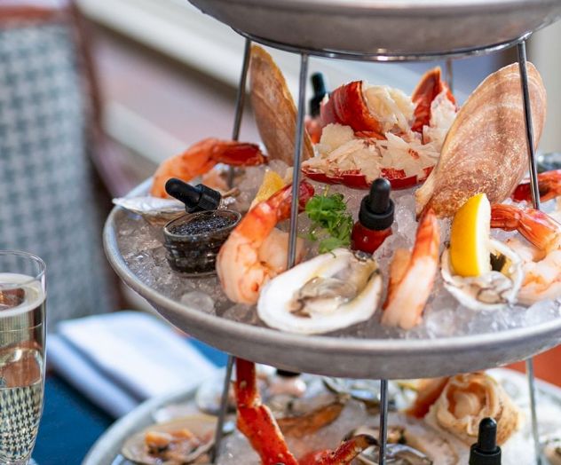 A three-tiered seafood platter featuring oysters, shrimp, crab legs, and mussels, accompanied by lemon wedges and sauce bottles.