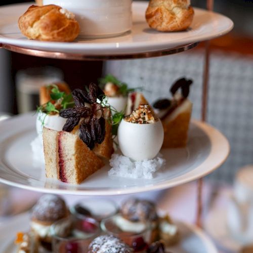 A three-tiered stand with assorted pastries and sandwiches, including cones, cakes, and puffs, presented elegantly.