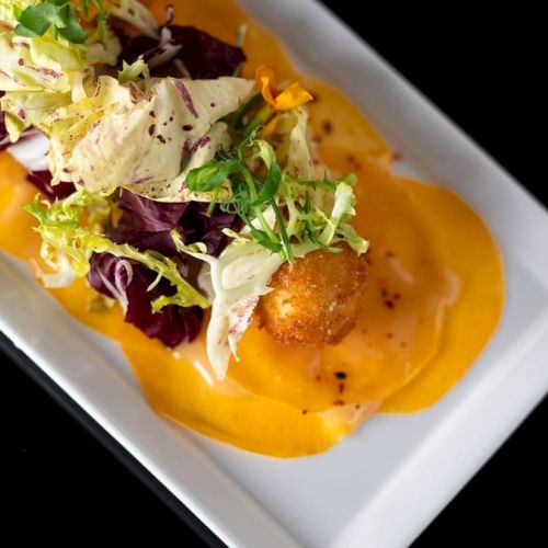 A gourmet dish featuring sliced yellow beets, greens, and fried cheese balls on a white rectangular plate.