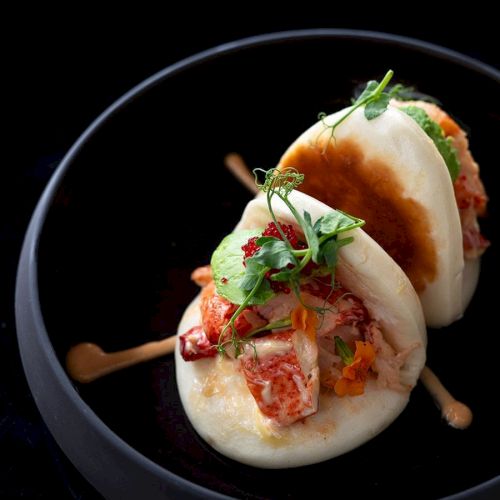 The image shows a dish of bao buns stuffed with chicken and topped with herbs, served in a black bowl.